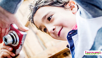 Niño mirando a la pantalla de su cámara digital preparada para hacer una fotografía. Imagen desde perspectiva contrapicada (de abajo hacia arriba)